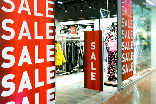 Big showcase window of sport store with dummy mannequin and white on red SALE close-up advertisement text, with reflections in mall