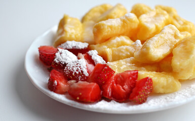 lazy dumplings with fresh strawberries and powdered sugar on a white saucer