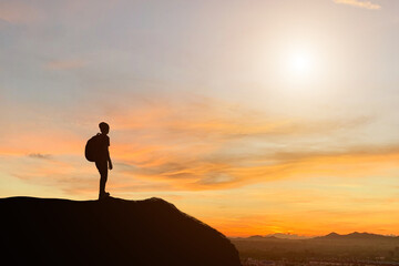 Silhouette of young traveler and backpacker standing and watched beautiful view sunset alone on top of the mountain. He enjoyed traveling and was successful when he reached the summit.