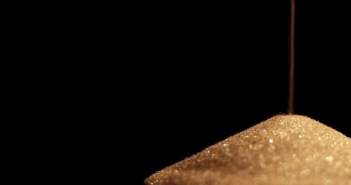 Hourglass. Sands move through hour glass. Sandglass close-up on a black background. Slow motion video. A pile of Golden sand at the bottom of the hourglass, small grains of sand fall from above.