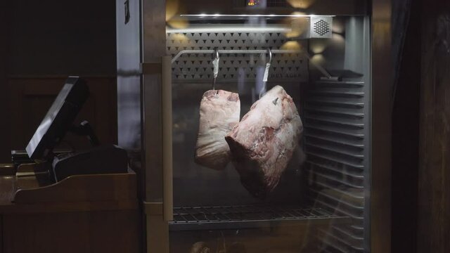 arge pieces of meat are hanging in the refrigerator in the store. close-up