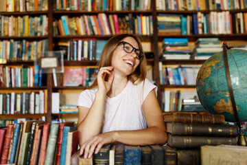 Young smiling attractive college girl portrait with eyeglasses standing in library, holding books .Education concept