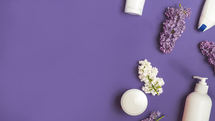 Cosmetic products and lilac flowers on violet background, flat lay. Beauty and care concept. space for text