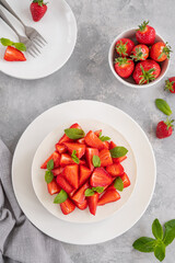 No baked cheesecake with fresh strawberries and mint on top on a white plate on a gray concrete background. Copy space.
