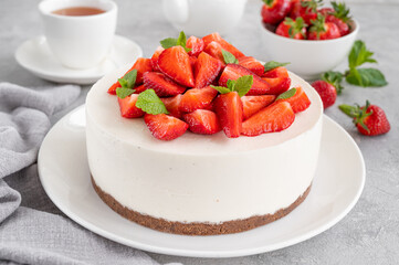 No baked cheesecake with fresh strawberries and mint on top on a white plate on a gray concrete background. Copy space.