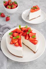 No baked cheesecake with fresh strawberries and mint on top on a white plate on a gray concrete background. Copy space.