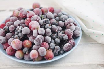 Frozen berries fruits background in ceramic plate close up.Fruits with frost. on vintage white wooden planks, blank space for text, copy space