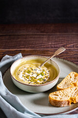 Food photography of a vegan pumpkin cream soup and bread with selective focus. Vegetables recipe. An autumn puree of seasonal products on a wooden table with vintage look.