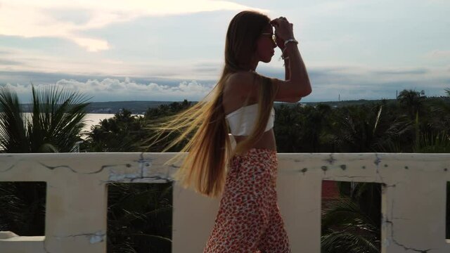 Beautiful redhead young female with white bikini top and dress walking on rooftop