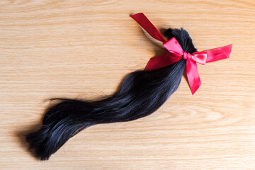 Mechón de pelo cortado anudado con un lazo de raso rojo sobre un fondo de madera. Donación de cabello para pelucas para pacientes con cáncer
