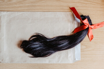 Mechón de pelo cortado anudado con un lazo de raso rojo metido en un sobre de color marrón. Enviar una donación de cabello para pelucas para pacientes con cáncer mediante carta