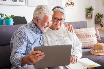 Fototapeta premium Two senior people stay at home looking together at laptop. An elderly couple, prevention and positivity concept