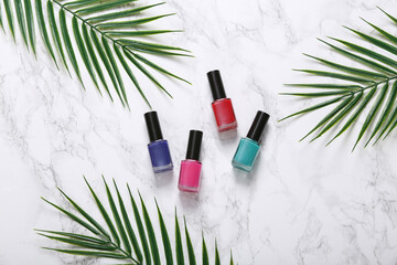 Bottle of nail polish and palm leaves on a marble background. Beauty flat lay