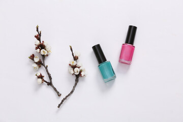 Nail pilish bottles and beautiful white flowering branches on white background. Springtime, beauty concept. Flat lay, top view.