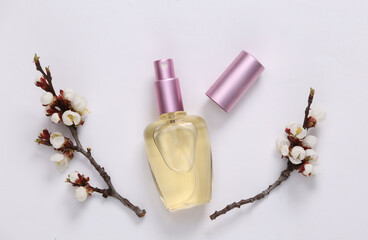 Perfume bottle and beautiful white flowering branches on white background. Springtime, beauty concept. Flat lay, top view.