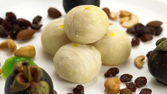 Rotation of chinese pastry or bean cake filled with sweet pasted mung bean and salted egg yolk with almonds, cashew nuts, raisins, kiwi and mangosteen on white background.