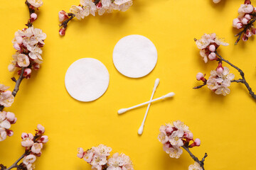 Hygienic cotton pads and ear sticks on yellow background with flowering branches. Hygiene concept
