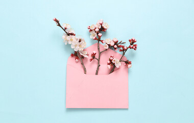 Envelope with beautiful flowering branches on blue background. Flat lay, top view.