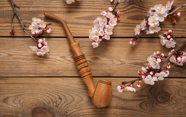 Obraz na płótnie Canvas Smoking pipe with beautiful pink flowering branches on wooden background. Flat lay, top view