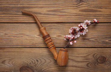 Smoking pipe with beautiful pink flowering branches on wooden background. Flat lay, top view