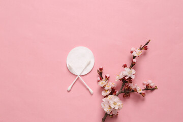 Hygienic cotton pads and ear sticks on pink background with flowering branches. Hygiene concept