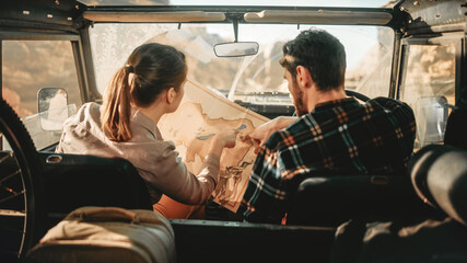 Happy Couple of Tourists Choosing Path with a Map while Driving Off Road SUV, Riding Through the...