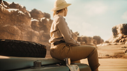 Desert Road Trip: Beautiful Female Traveler Looking Around while Sitting on a Hood of Her Offroad SUV, Planning Route full of Wonder and Exploration. Woman Adventurer Traveling Through Canyon © Gorodenkoff