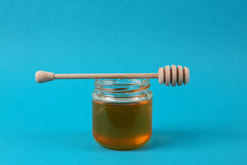 Bee honey jar and honey wooden spoon on blue background