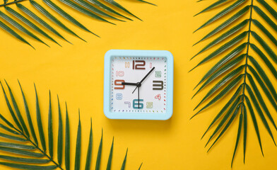 Alarm clock and palm leaves on yellow background. Time to Travel. Tropical composition. Top view. Flat lay - Powered by Adobe