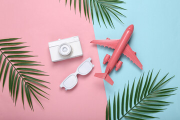 Air plane, camera, sunglasses and palm green leaves on pink blue pastel background. Travel concept....