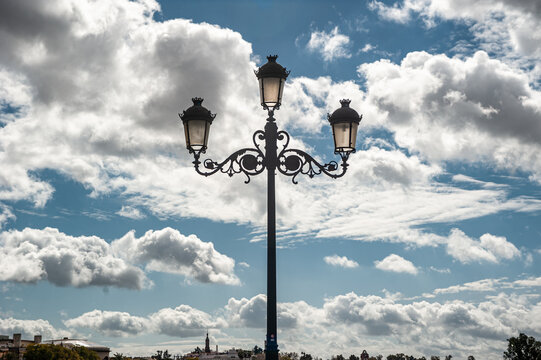 Photograph taken of the lamppost of the Isabel II bridge, Triana bridge, and the Guadalquivir river in Seville, with a cloudy sky of storm