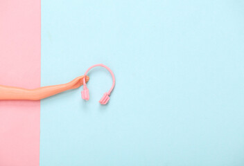 Doll hand holding headphones on blue-pink pastel background. Minmalism, concept art. Copy space