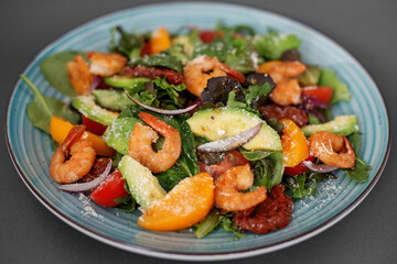 Fresh salad plate with shrimp, tomato and mixed greens (arugula, mesclun, mache) on wooden background close up. Healthy food. Clean eating.