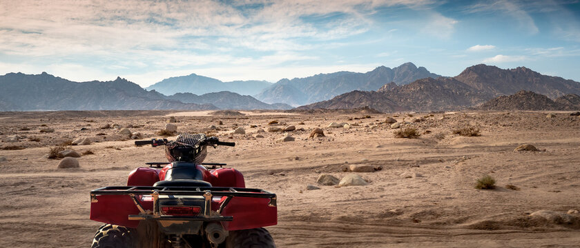 Desert safari on a quad bike in Sharm-el-Sheikh, Egypt. Off road driving in a stone desert with silhouettes of mountain hills.
