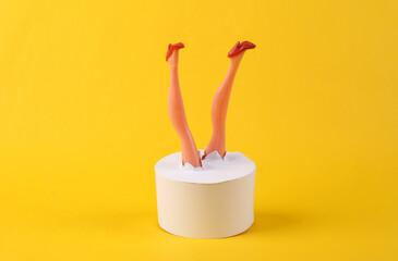 Doll's legs through a torn cylinder on a yellow background. Minimalism