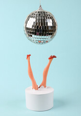 Doll feet and disco ball on a blue background. Minimalistic party concept.