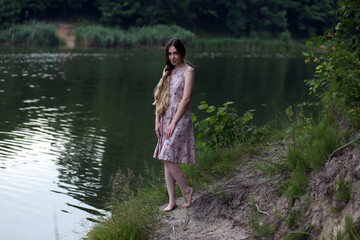 Fototapeta na wymiar Long haired woman in pink dress standing near water