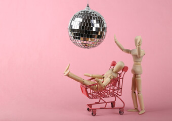 Two puppets in shopping trolley under disco ball on pink background. Minimalism party concept
