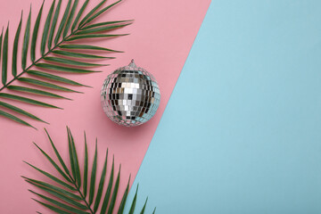Disco ball with palm leaves on a blue-pink background. Top view. Flat lay. Minimalism party concept