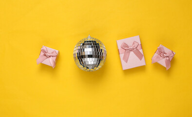 Disco ball and gift boxes on yellow background. Minimalism party and holiday concept