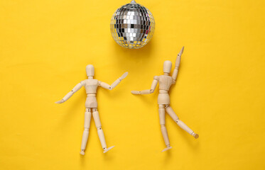 Two puppets dancing under disco ball on yellow background. Minimalism party concept. Top view