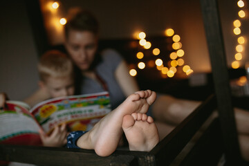 Mom and son reading a book. Boy's feet on foreground. Image with selective focus