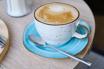Сup with cappuccino coffee on a round wooden table. Shallow depth of field