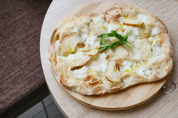 Roman round pizza five or four cheeses with baked pear on a round wooden kitchen pizza board. Delicious fresh Italian pizza on a round wooden table. Selective focus