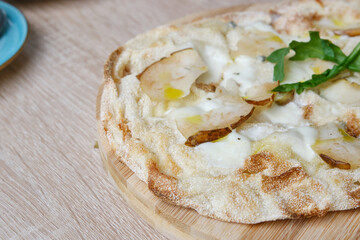 Roman round pizza five or four cheeses with baked pear on a round wooden kitchen pizza board. Delicious fresh Italian pizza on a round wooden table. Selective focus