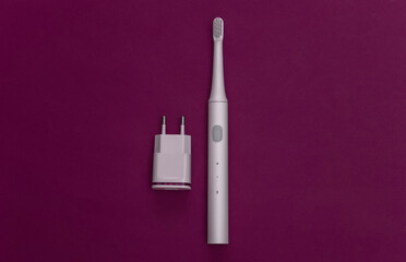 Electro-toothbrush with charger on purple background. Top view