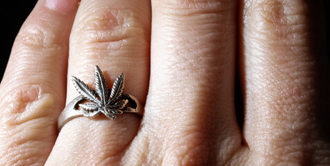 Close-up of a silver ring in the form of a marijuana leaf worn on a hand. White gold jewelry. Drug addiction symbol. Illegal distribution of harmful substances. Sign. Banner. Copy space. Dealer sign