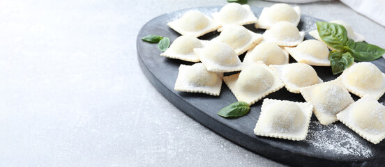 Homemade uncooked ravioli and basil on grey table