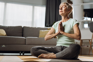 Senior woman sitting in Lotus position and meditating at home