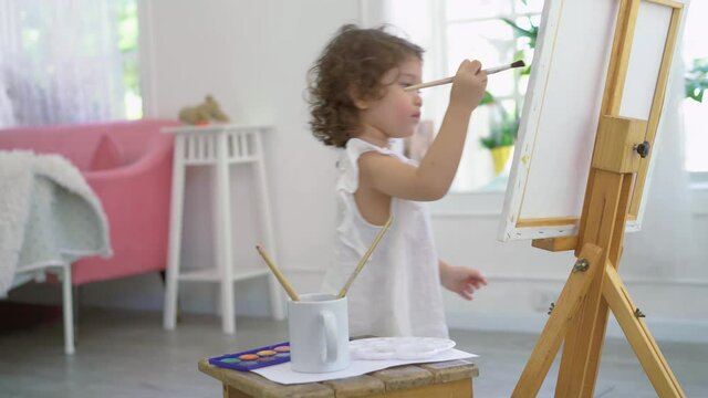 A little cute girl artist painting picture on canvas with watercolor paints at home